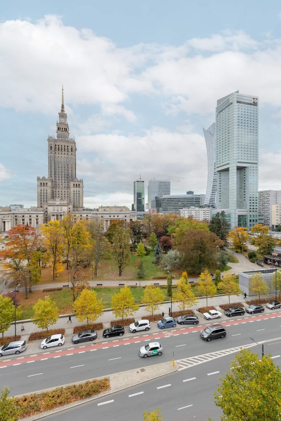 A vertical perspective of the Warsaw skyline with iconic landmarks and tree-lined streets.

