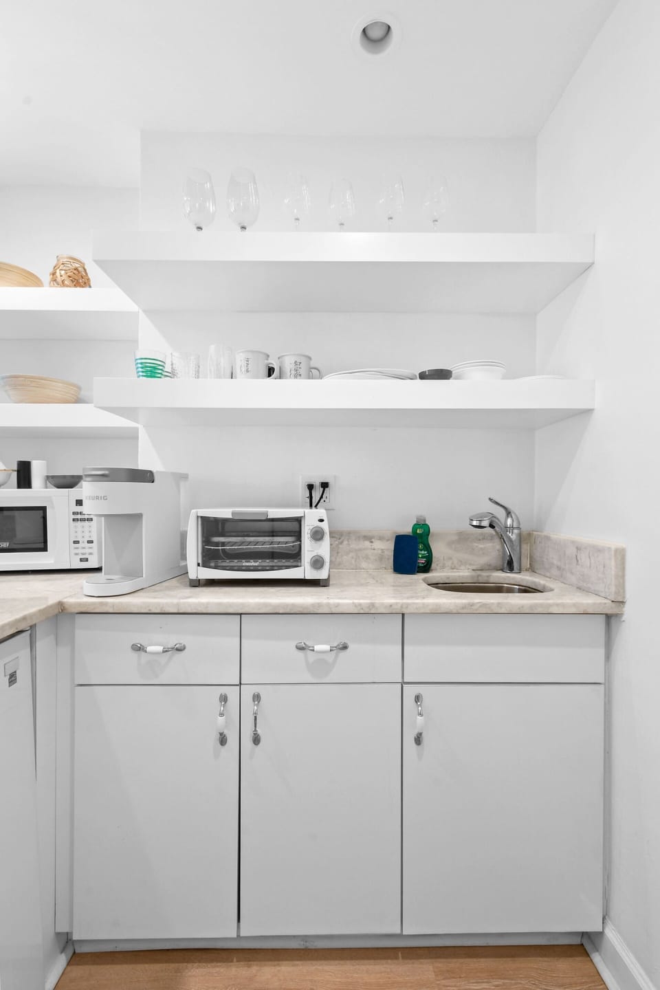 Kitchenette with a Toaster oven, microwave, mini fridge, Keurig coffee maker, glasses, plates, and cutlery.