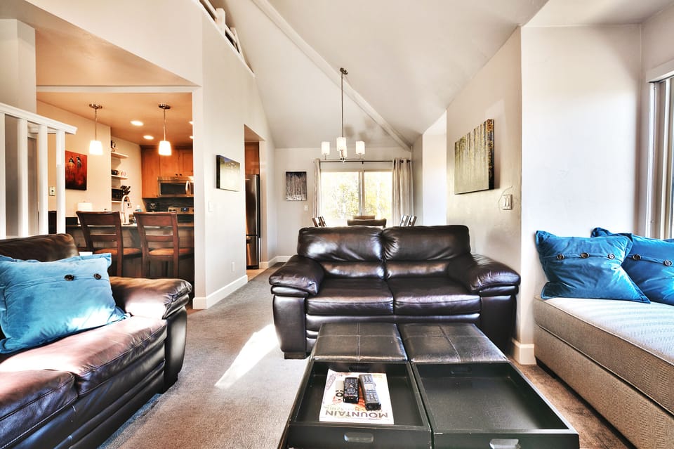 - Open layout connects living area with kitchen and dining space  
- Leather seating and plush pillows create a welcoming lounge  
- Vaulted ceilings and natural light enhance the mountain getaway