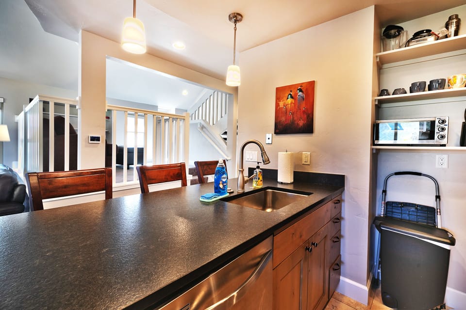 - Kitchen with breakfast bar and seating for three  
- Stainless sink and modern fixtures with bright lighting  
- Open shelves stocked with mugs and essentials