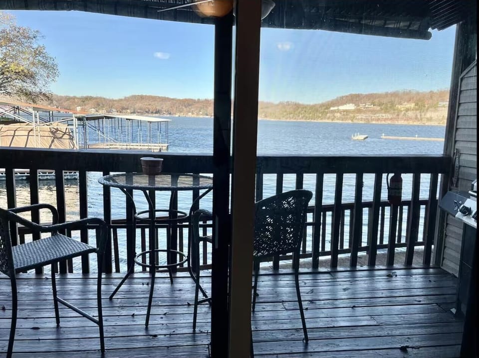 Wooden balcony with chairs and a round glass-top table overlooking the lake.