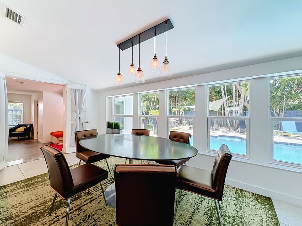 Open dining area with Edison pendant lights and poolside views, beside the kitchen.