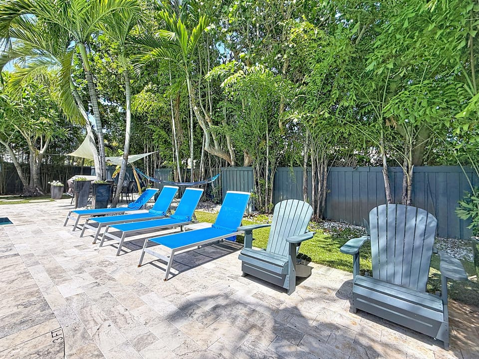 Travertine sun deck with cushioned chaise loungers and Adirondack chairs by the pool.