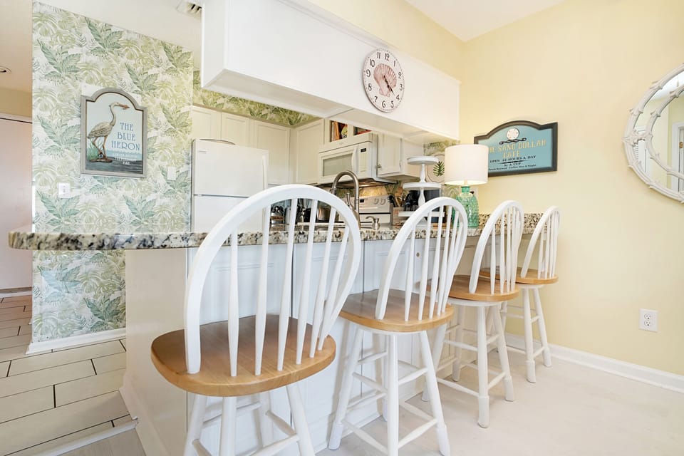 Gather around your bright kitchen island for morning coffee or casual meals in this coastal-themed space with charming tropical wallpaper.
