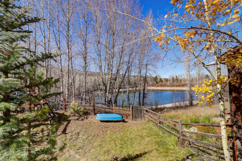 A tranquil backyard borders a serene lake, surrounded by leafless trees and wooden fencing. A canoe rests on the grass under a clear blue sky.