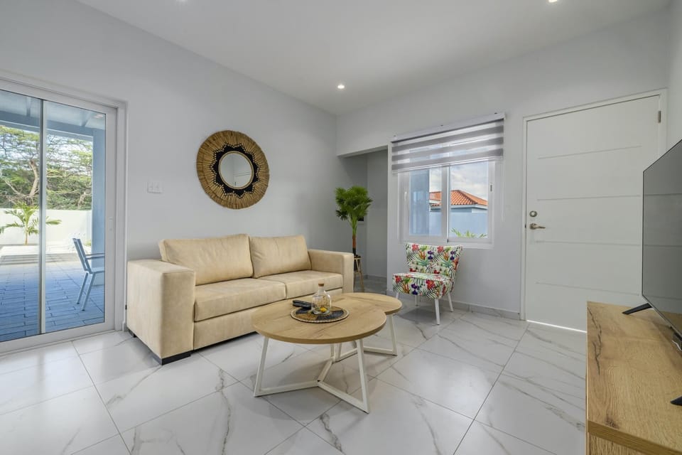 This living room area has a comfy sofa, large TV and modern wooden center table. The white wall and neutral colored furniture creates a very cozy and a relaxing gathering space.