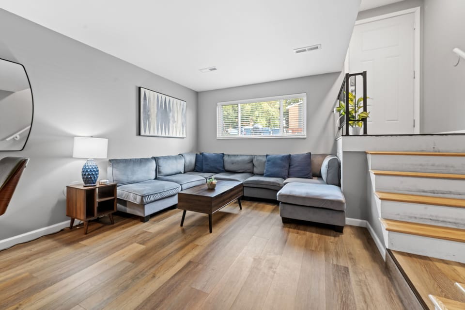 A large blue sectional wraps around a wood coffee table beside the living room window and staircase.