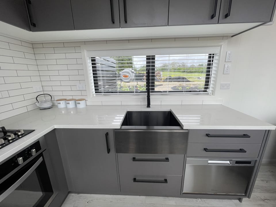 Modern kitchen with subway tiles / butler sink / dishwasher and stone bench