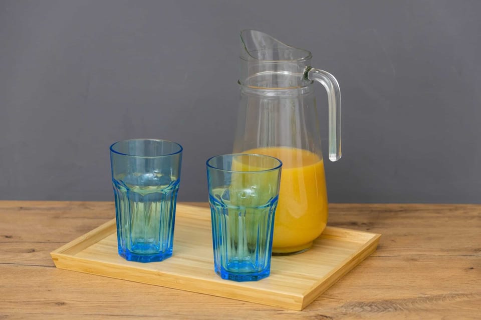 A wooden tray with two glass cups and a glass jug filled with orange juice, placed on a wooden countertop.
