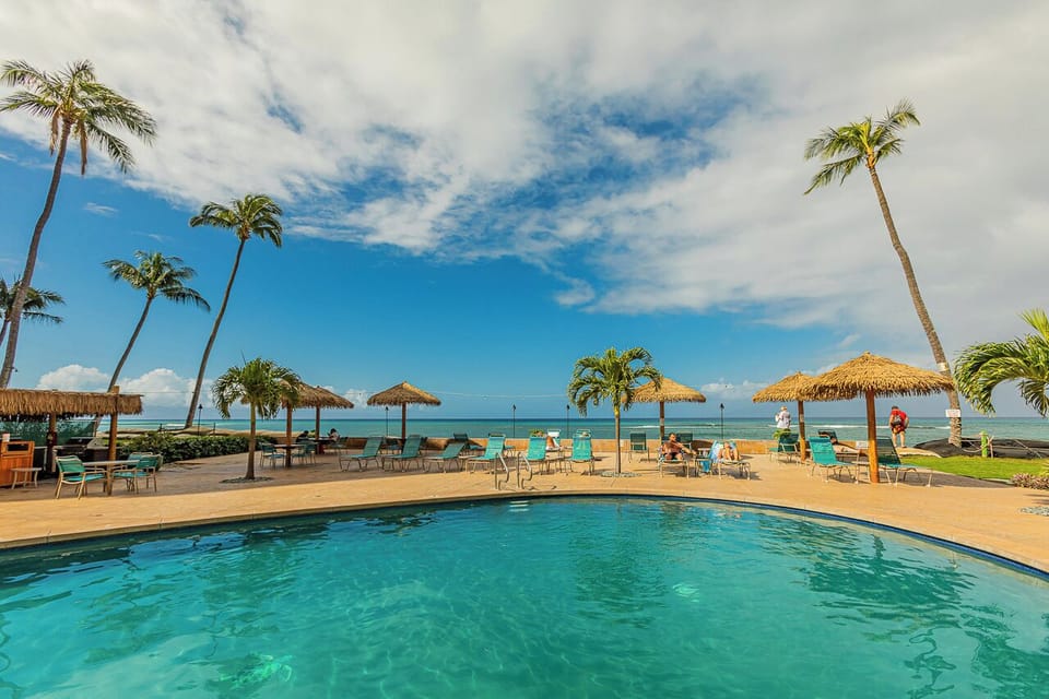 The beachside pool opens to turquoise waters and swaying palms, with thatched umbrellas and lounge chairs dotting the shoreline.