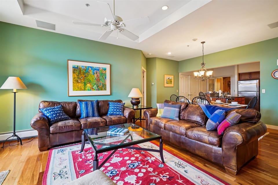 Bright living room with mountain views, leather seating, and a stone fireplace. Step out through the French doors to the deck with red Adirondack chairs and take in the Vermont scenery.