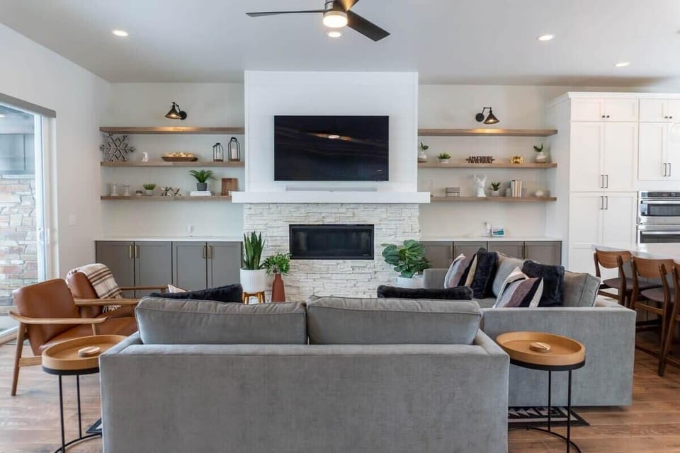 The living room is set up with everything you need for a relaxing space with an electrical fireplace, 65” smart TV, two sofas and two chairs, and well-placed decor creating a cozy home ambiance.