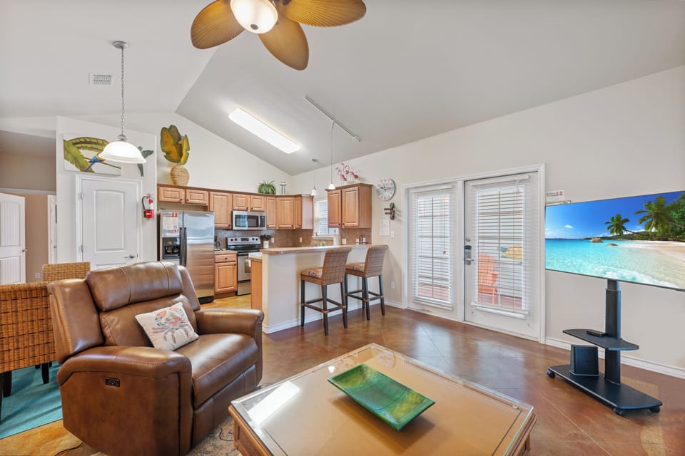 Relax in your open-plan living space with leather recliners, tropical ceiling fans, and a fully equipped kitchen—perfect for your beach getaway.