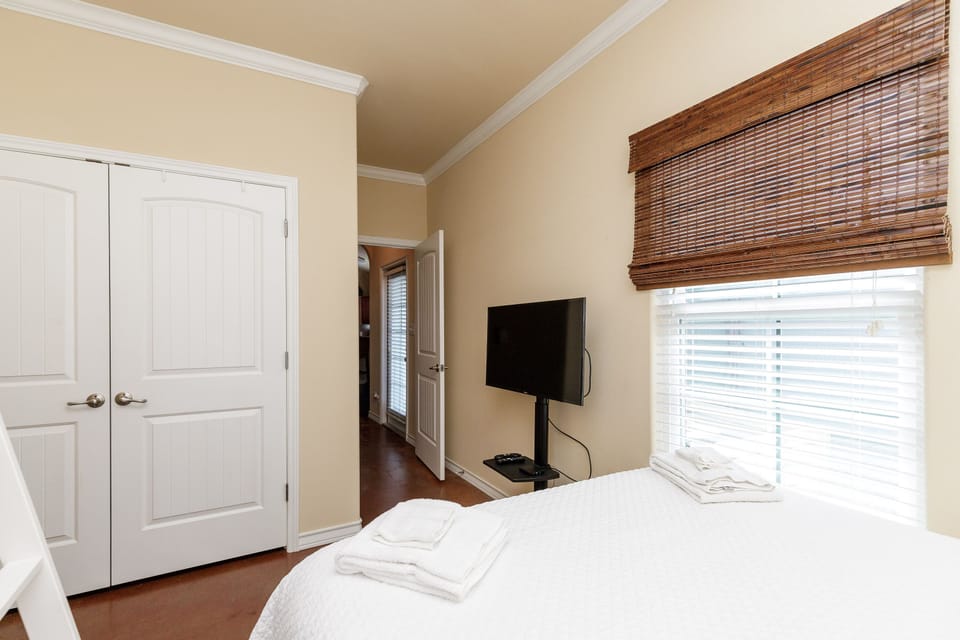 Your peaceful bedroom features a comfortable bed, flat-screen TV, and warm bamboo blinds that filter natural light beautifully.