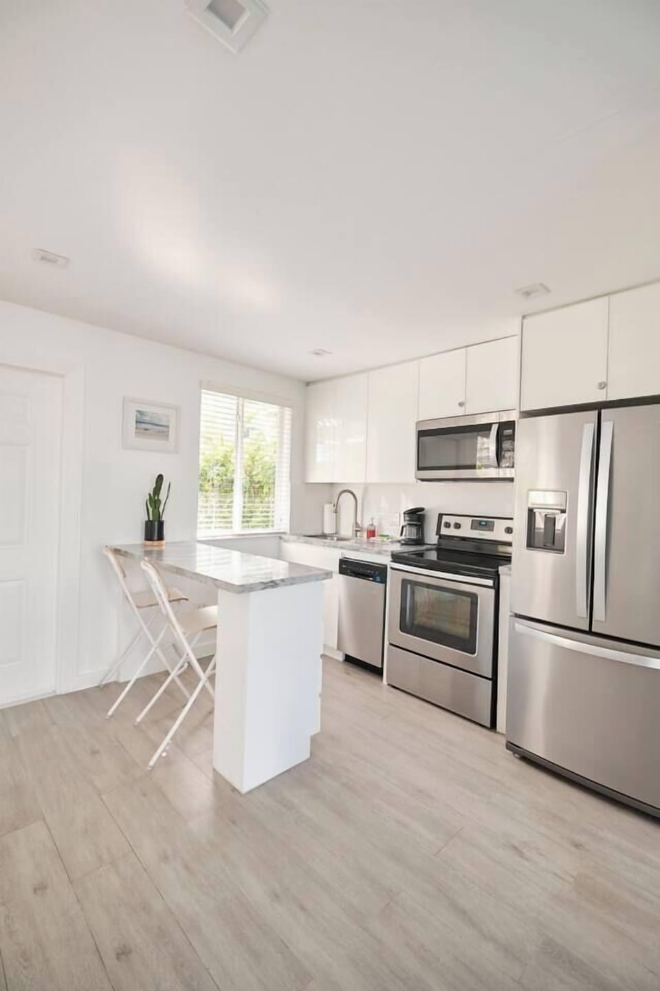 Sleek white kitchen with minimalist design, stainless steel appliances, and marble countertops. Counter can also be used as work space.