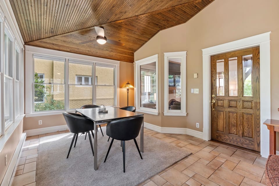 Your sunlit dining space features rustic wood ceilings, elegant furnishings, and charming neighborhood views through large windows.