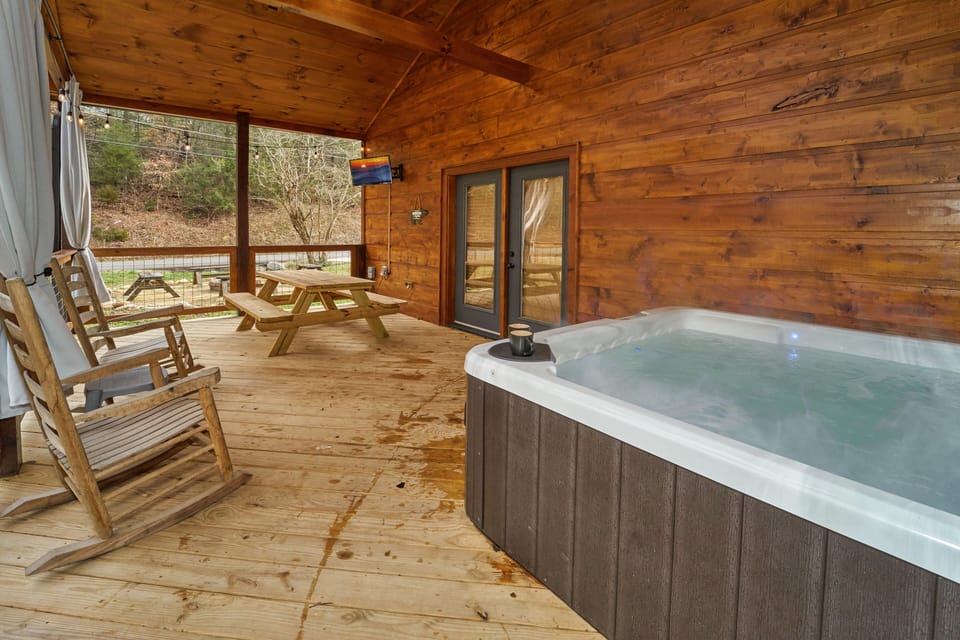 Covered patio, complete with hot tub, rocking chairs, picnic table, & Smart TV 