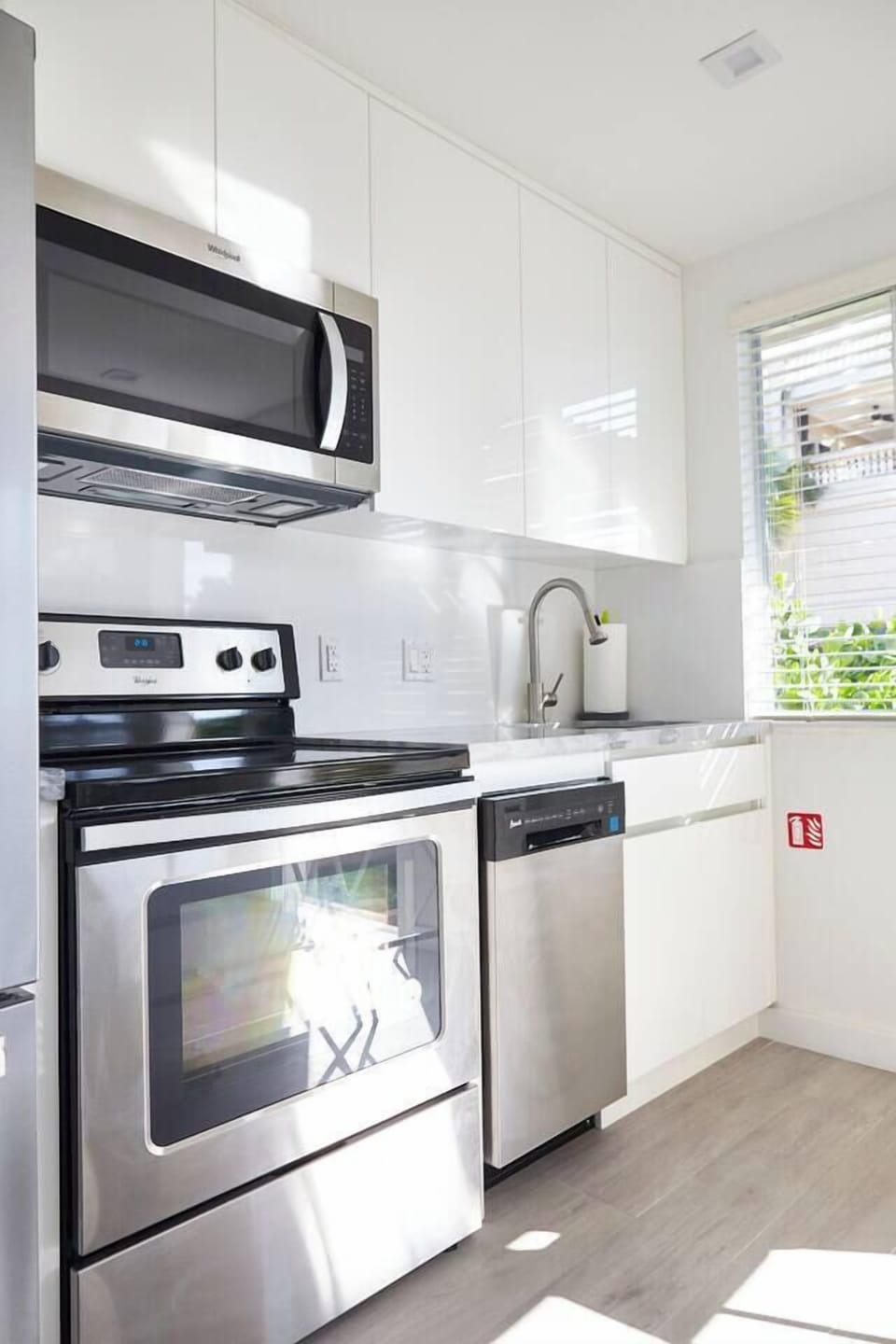 Sleek white kitchen with minimalist design, stainless steel appliances, and marble countertops. Counter can also be used as work space.