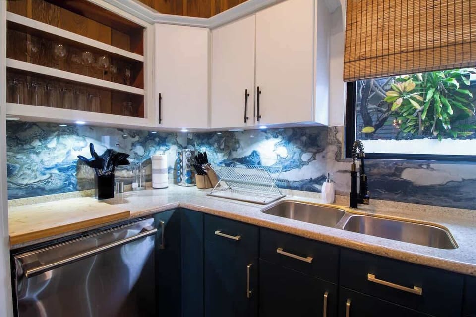 The kitchen features deep blue cabinetry contrasted w/ white upper cabinets & gold hardware. Boasts a unique marble backsplash, complementing the rich wooden accents above. Equipped with modern stainless steel appliances and everything you need.