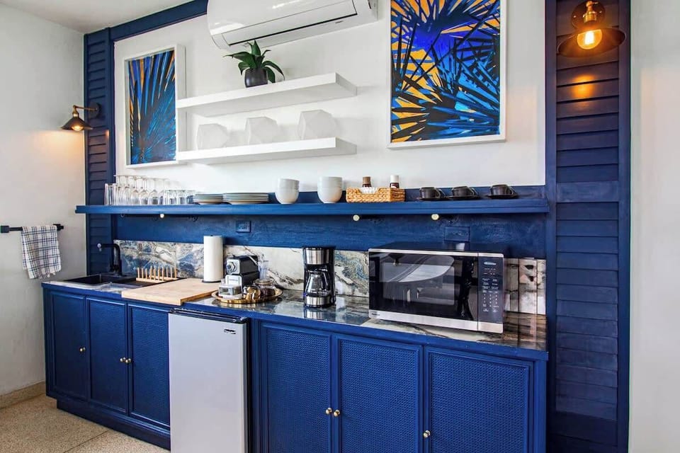 Second floor living room with dining table and stools with views of the ocean. Kitchenette equipped with coffee maker, espresso machine, mini-fridge, and microwave. Also, coffee cups, plates, small sink, and wine glasses.