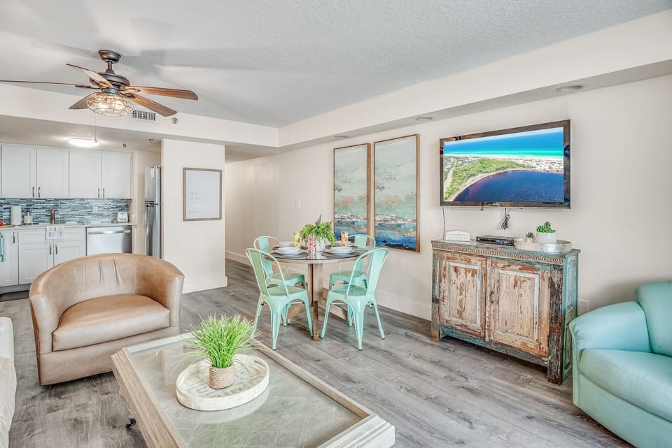 Relax in your coastal-inspired living space with turquoise accents, modern kitchen, and beach views on the TV screen.