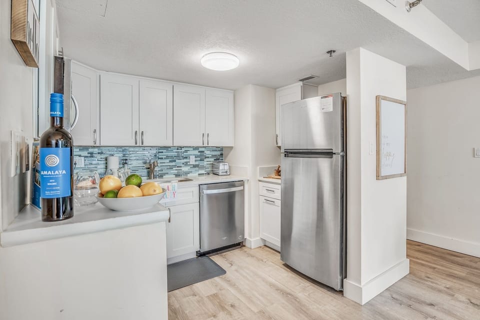 Your fully equipped kitchen welcomes culinary adventures with gleaming stainless steel appliances, crisp white cabinetry, and stunning blue backsplash.