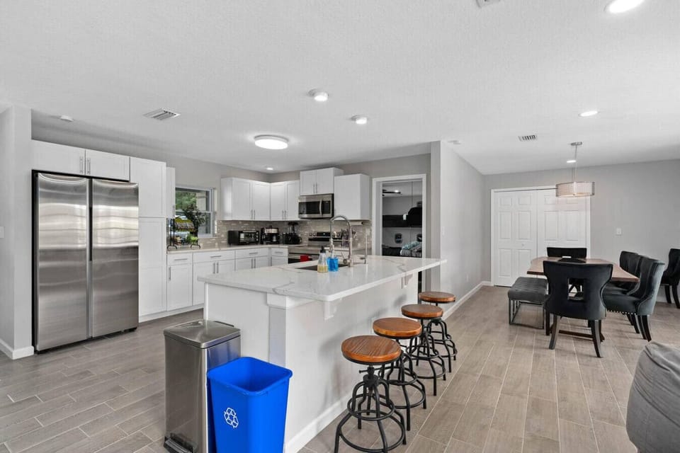 Open-concept kitchen with white shaker cabinets, large quartz island, bar stools, stainless fridge and dining area, Orlando
