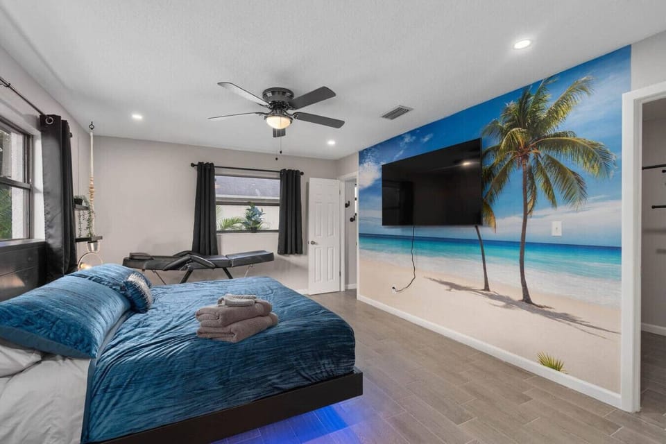 Beach-themed bedroom with blue velvet bedding, tropical palm and ocean mural wall, ceiling fan and flat-screen TV, Orlando