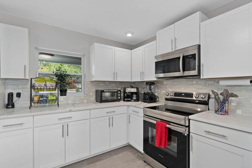 Well-equipped kitchen with white cabinets, electric range, stainless microwave, black appliances and large window, Orlando