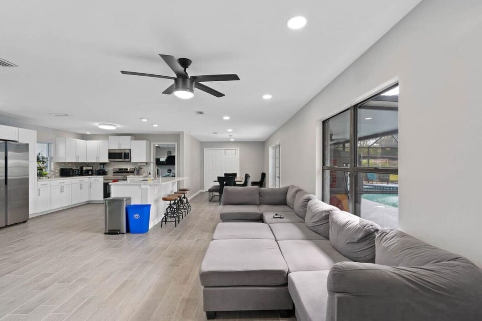 Spacious open-concept living room with gray sectional, ceiling fan, kitchen island with bar stools and pool view doors, Orlando