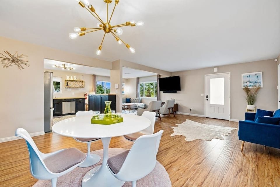 Bright open-plan dining and living with tulip table, sputnik chandelier, and wet bar nook — mid-century Palm Springs vibes from the moment you walk in