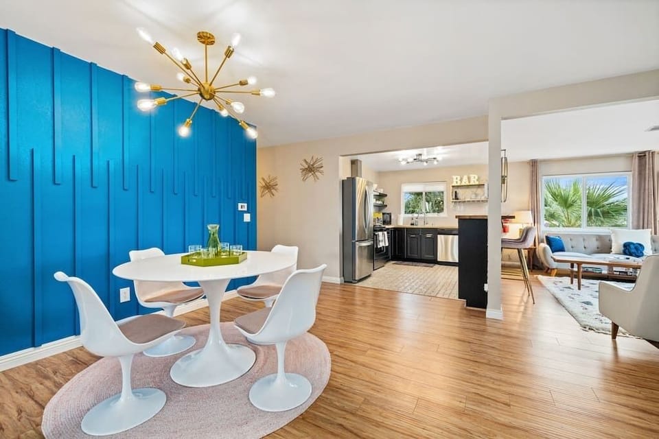 Sunlit open-plan dining with tulip table, cobalt statement wall & sputnik chandelier — midcentury modern done right.