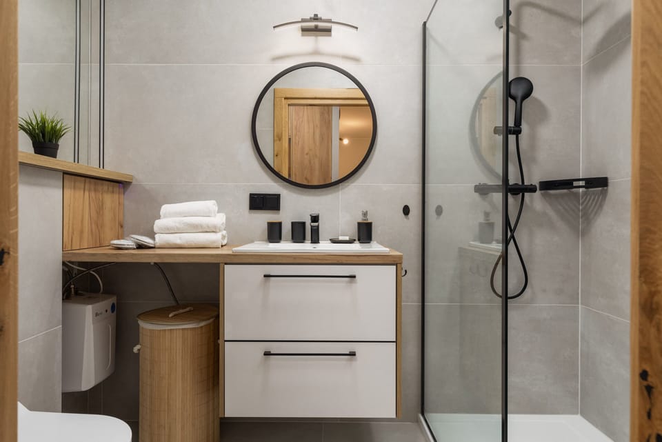 A bathroom with a modern design, featuring a circular mirror and sleek fixtures.
