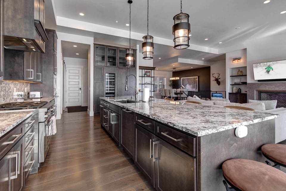 A spacious kitchen with granite countertops and modern industrial lighting flows seamlessly into a cozy living area, creating the perfect spot to cook, gather, and relax together.