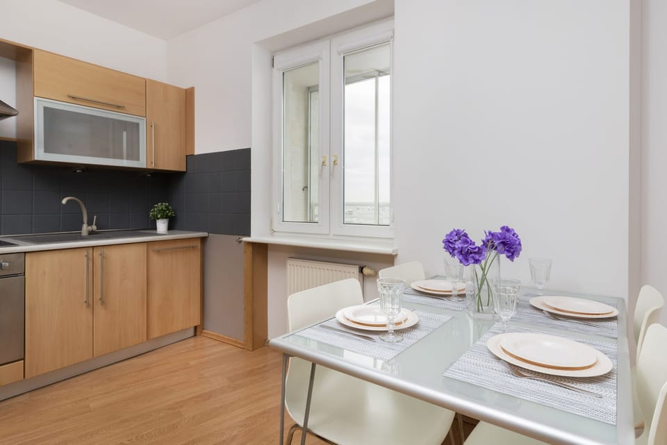 A small dining table setup with plates and a vase with purple flowers.
