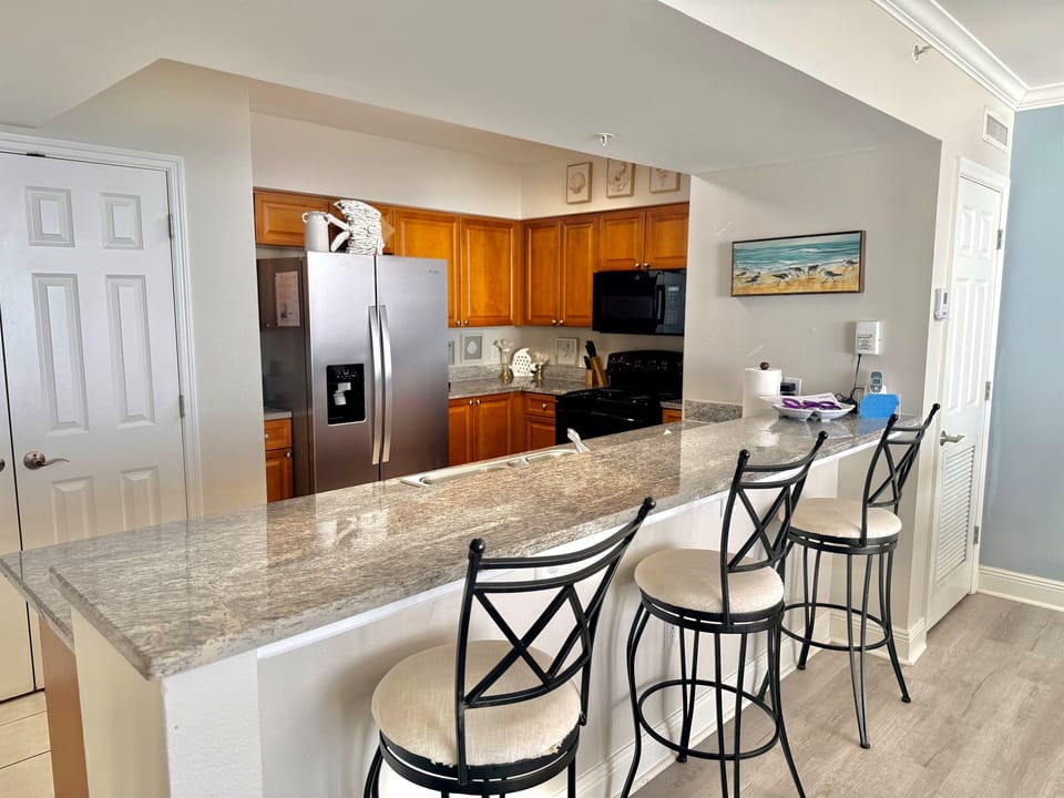 Fully Equipped Kitchen — Granite counters, a brand-new 2026 stainless steel refrigerator, and breakfast bar seating.