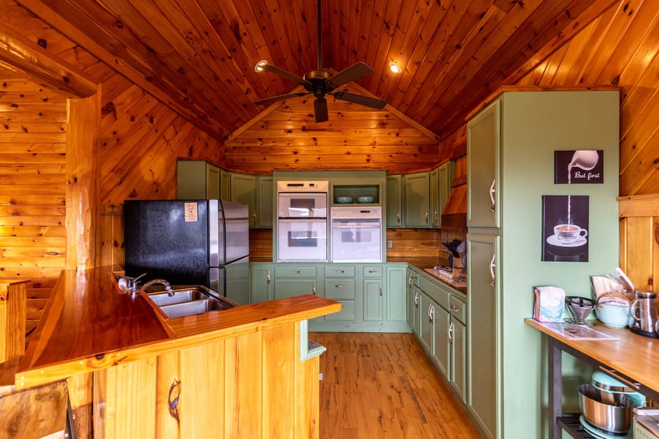 Sage green cabinets and warm pine wood fill the kitchen at River View Retreat, a cheerful space ready for home-cooked mountain meals.