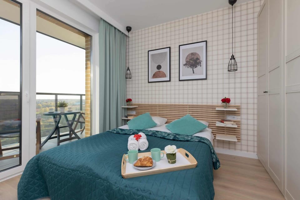 A neatly arranged bedroom with teal accents, including pillows and throws, complemented by a bookshelf and decorative wall art.