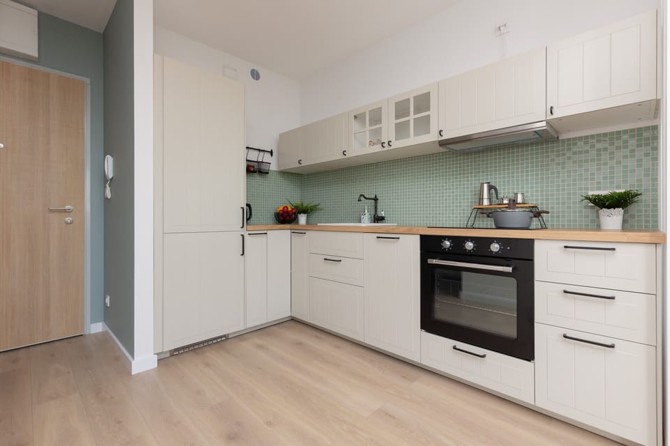 A fully equipped kitchen with white cabinets, a stove, and green mosaic backsplash tiles for a refreshing look.
