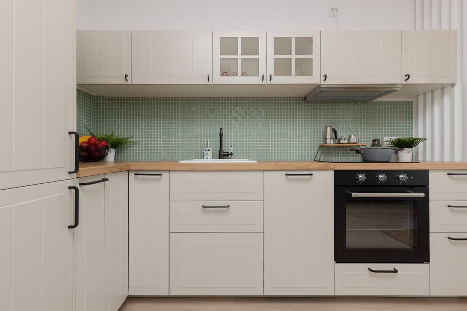 A fully equipped kitchen with white cabinets, a stove, and green mosaic backsplash tiles for a refreshing look.