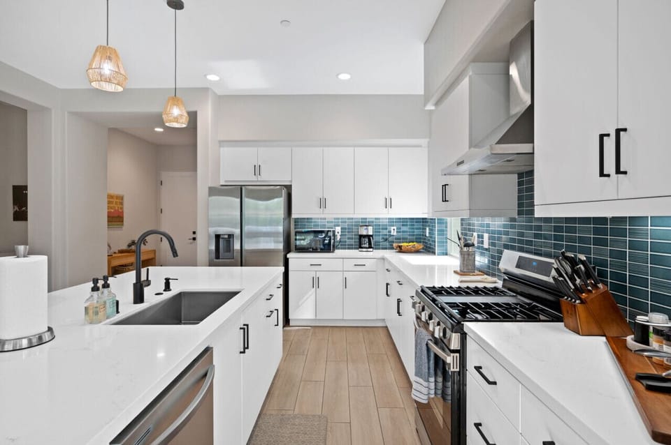 Bright kitchen w/ sleek cabinetry, stainless appliances & blue tile backsplash.