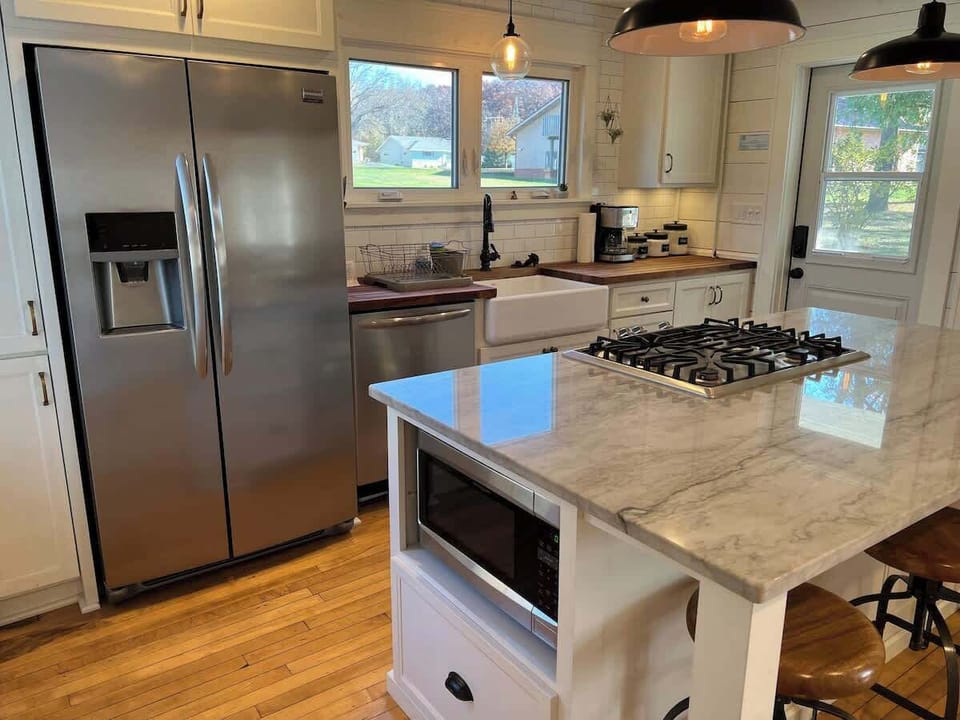 This kitchen includes a farmhouse sink overlooking the backyard, which provides natural lighting. It is finished with a butcher block countertop. stainless steel appliances, and gas stove. The kitchen island offers seating for a breakfast nook and space for cooking!