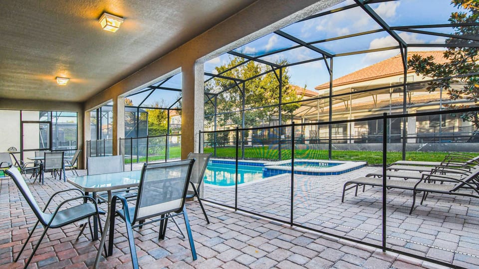 A covered patio with multiple dining sets overlooks a screened-in pool area with lounge chairs and a hot tub.