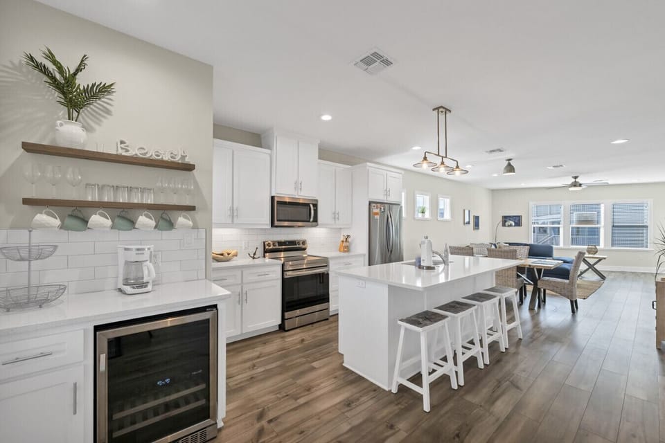 Light-filled coastal kitchen with large island, bar seating, and clean white finishes ideal for meals and entertaining.