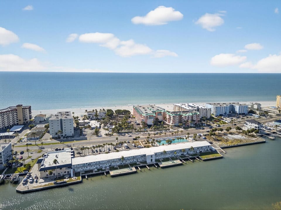 Sweeping aerial of waterfront buildings set between calm water & the open sea.