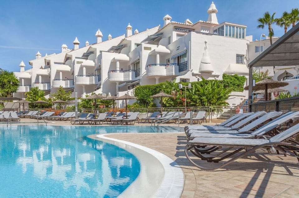 Curved pool surrounded by palm trees and white villas, an idyllic setting for leisure and relaxation.