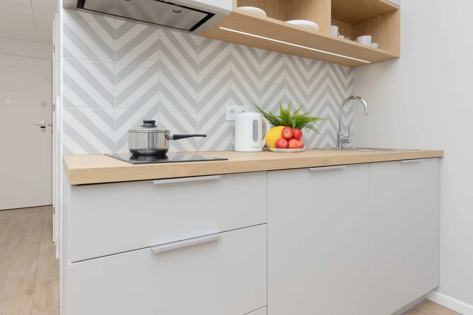 A compact and fully equipped kitchen featuring white cabinets, wooden countertops, and a geometric backsplash. The kitchen includes modern appliances and ample storage.
