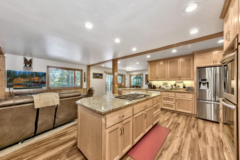 Kitchen with granite island cooktop, light wood cabinetry, stainless steel appliances, and wood-look flooring.