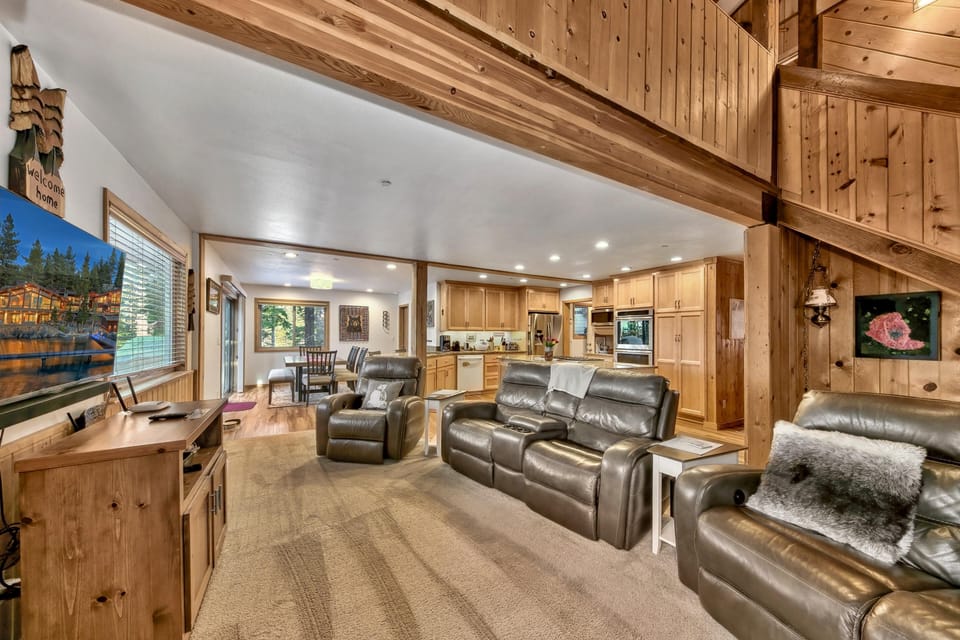 Living room open to the kitchen and dining area, featuring leather recliners, wood paneling, and recessed lighting.