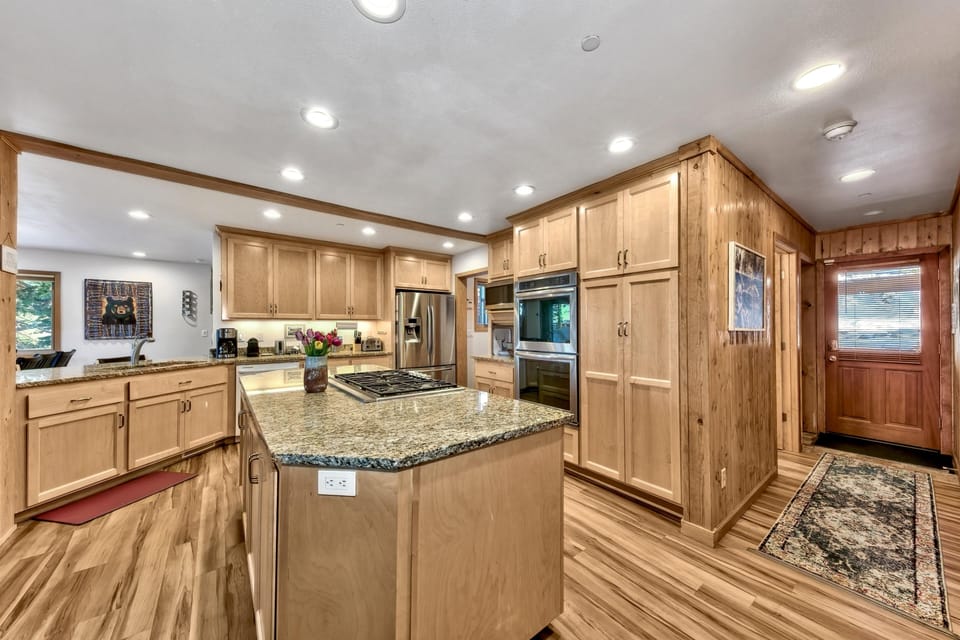 Kitchen island with gas cooktop and granite countertop, surrounded by light wood cabinetry and hardwood floors.